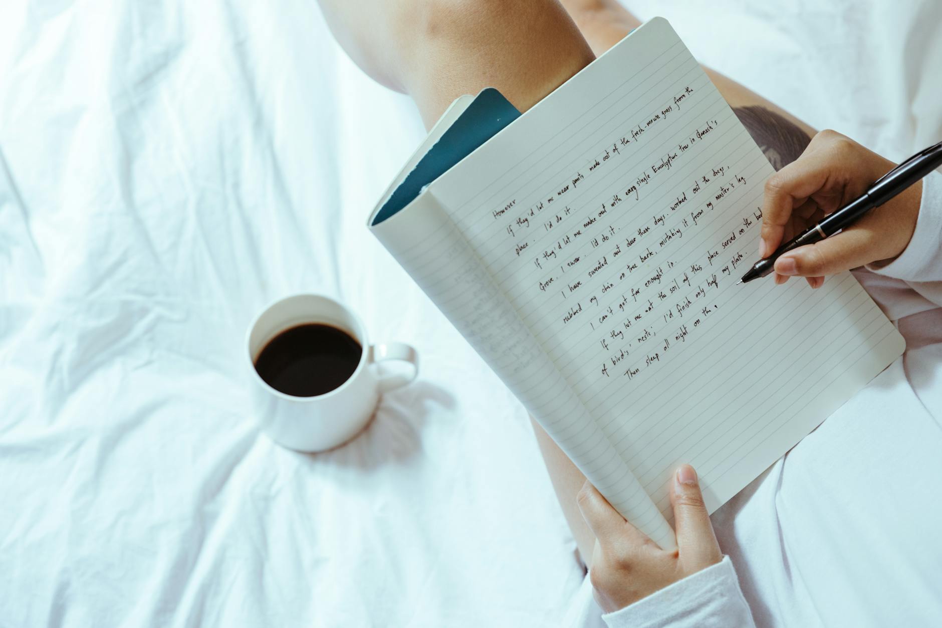 Woman sitting on bed with cup of coffee, writing in her notebook