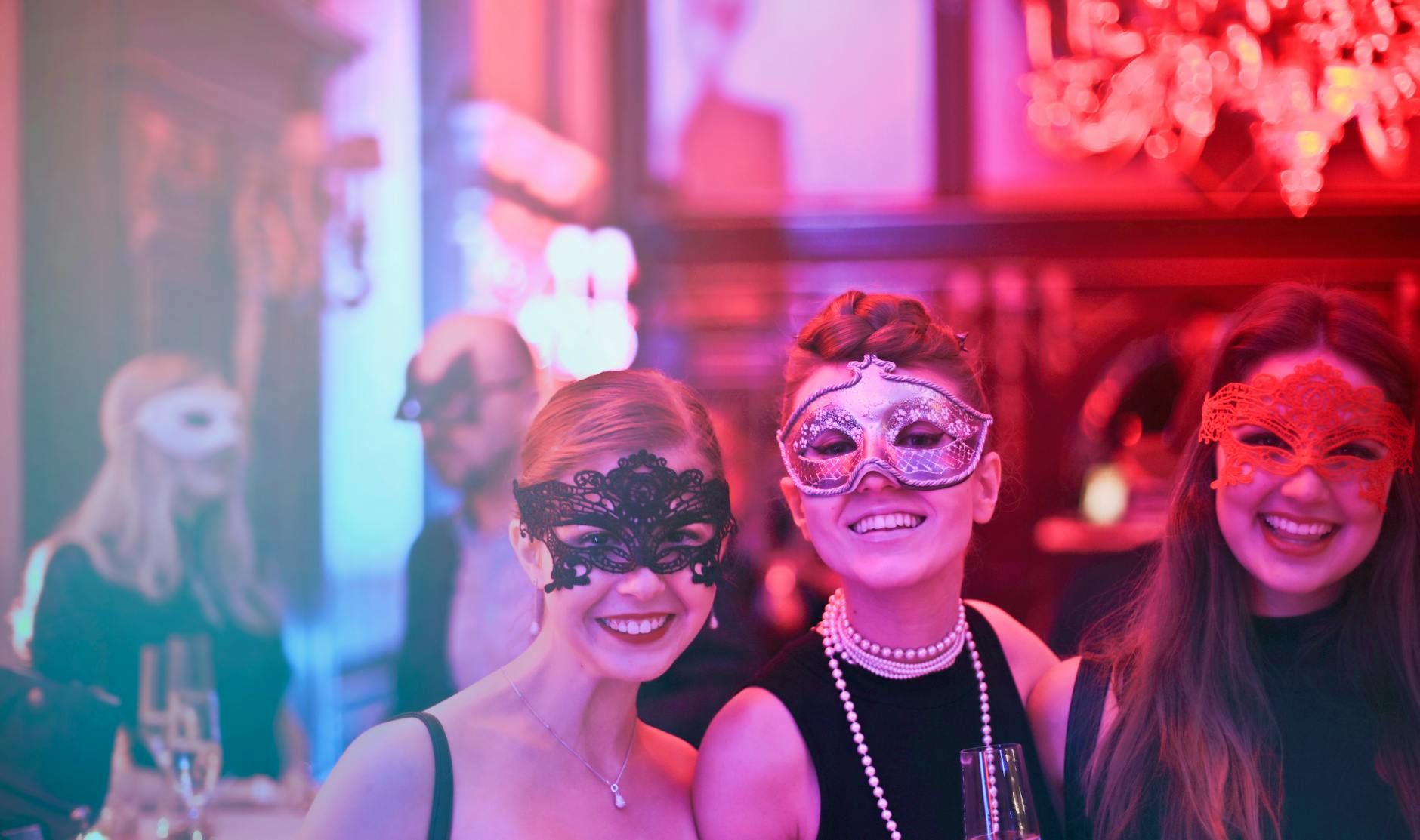 Three women in masks at a party, all smiling